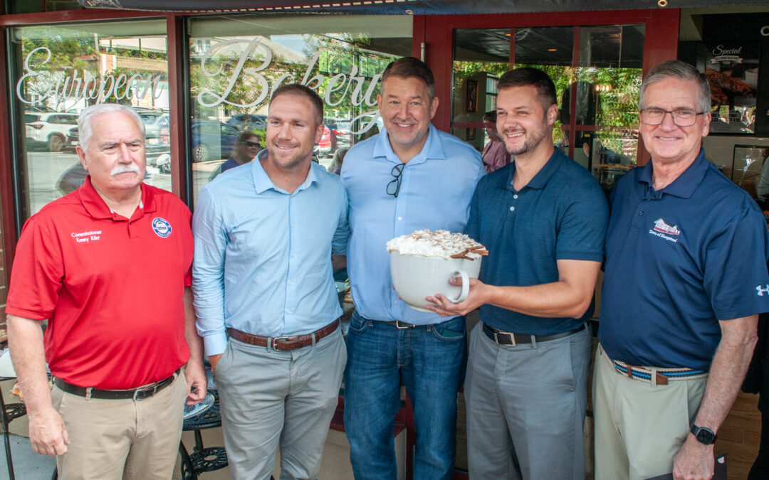 Five man standing in front while the other one is holding a large cup of a cappuccino.